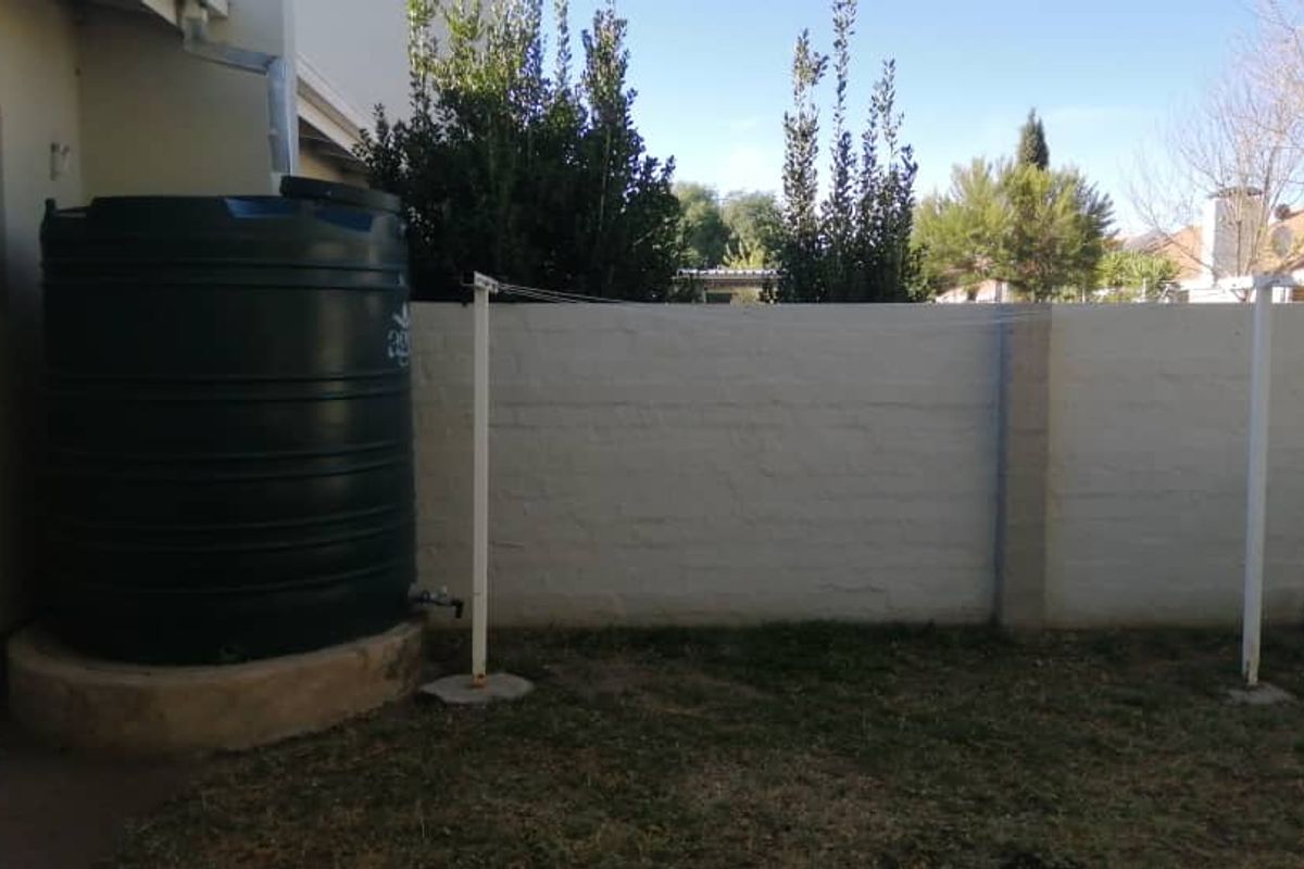 A rear garden area featuring a large water storage tank on a concrete base and a fixed metal washing line against a boundary wall.