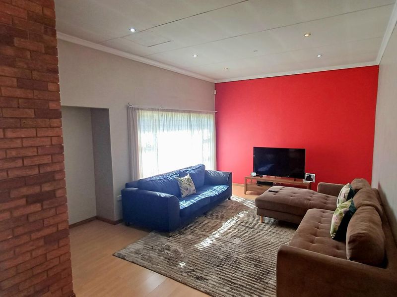 Spacious living room featuring laminate flooring, an exposed brick feature pillar, and recessed ceiling lighting, providing a comfortable and functional family space.