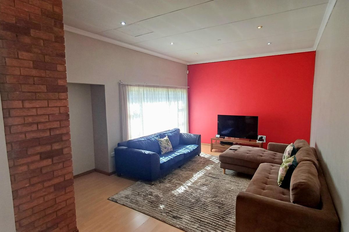 Spacious living room featuring laminate flooring, an exposed brick feature pillar, and recessed ceiling lighting, providing a comfortable and functional family space.