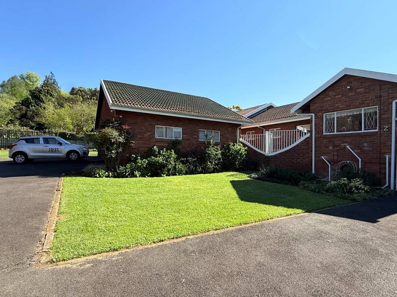 Front exterior view of a brick townhouse featuring a well-maintained lawn, paved driveway, and secure gated entrance.