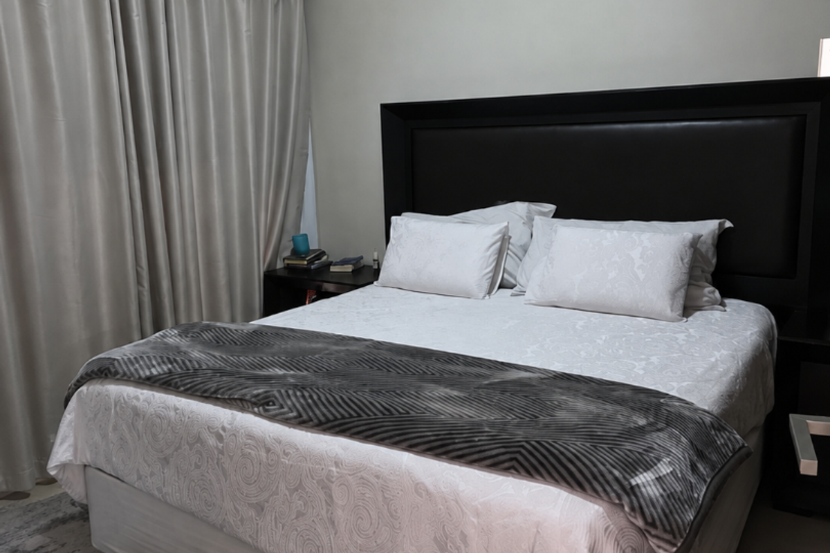 A well-maintained bedroom featuring tiled flooring, a wall-mounted split-system air conditioner, and neutral curtains.