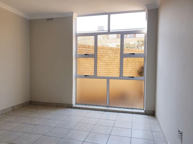 A bright, empty bedroom featuring neutral tiled flooring, clean walls, and large aluminium-framed windows providing natural light.