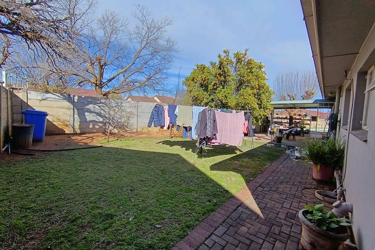 A rear garden featuring a paved walkway, lawn area, and perimeter boundary wall, providing a functional outdoor space.