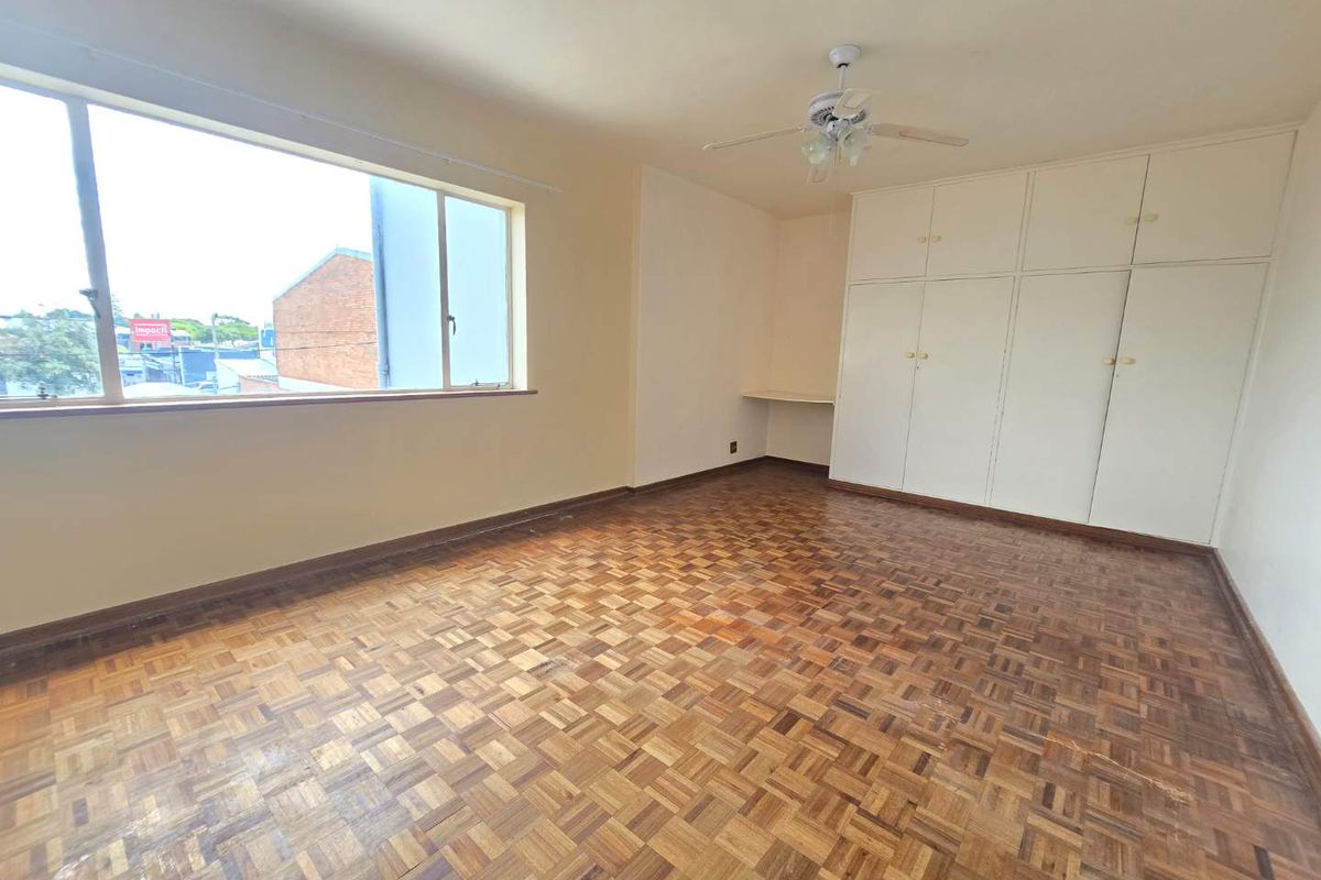 Spacious bedroom featuring original parquet flooring, extensive built-in cabinetry, and a ceiling fan, offering a blank canvas for personalization.