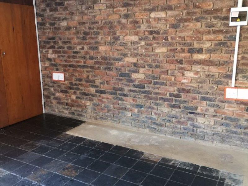 A garage space featuring an exposed brick wall, slate tile flooring, and a built-in wooden cupboard, showing signs of wear and dated finishes.
