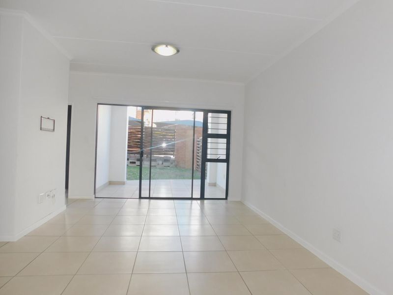 A bright, empty living room featuring neutral tiled flooring and a large sliding glass door providing access to an outdoor patio area.
