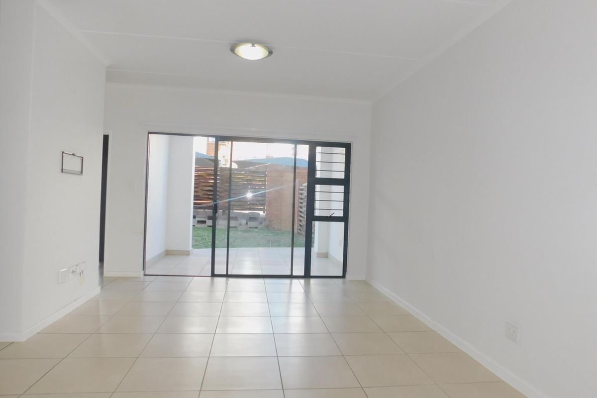 A bright, empty living room featuring neutral tiled flooring and a large sliding glass door providing access to an outdoor patio area.
