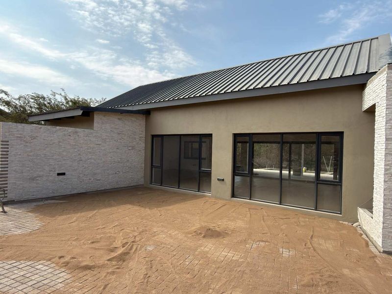 Rear exterior view of a modern home featuring stone cladding, a metal roof, and large sliding glass doors leading to an unfinished patio area.