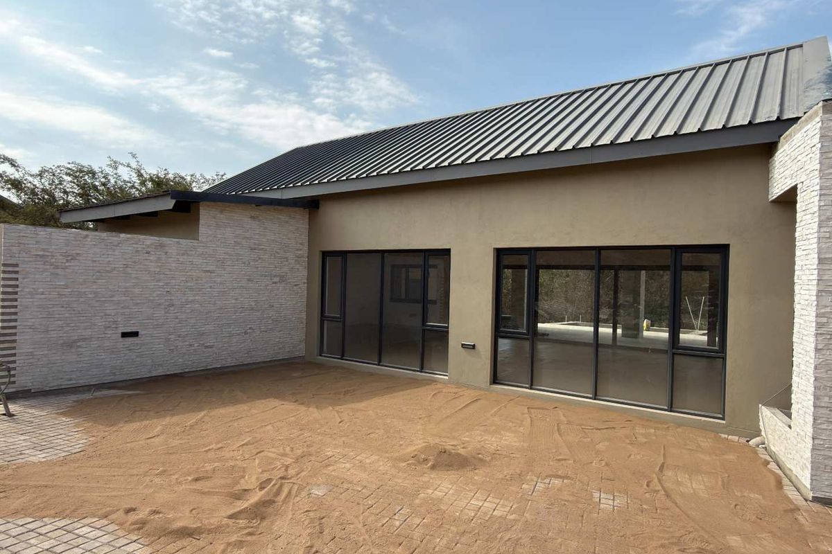 Rear exterior view of a modern home featuring stone cladding, a metal roof, and large sliding glass doors leading to an unfinished patio area.