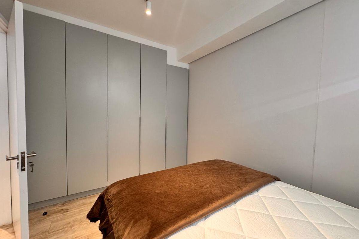 A clean bedroom featuring modern floor-to-ceiling built-in wardrobes, light laminate flooring, and minimalist track lighting.