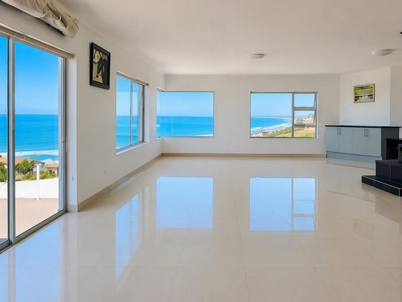 Spacious, light-filled living area featuring polished tile floors, a modern freestanding fireplace, and expansive windows offering panoramic ocean views.