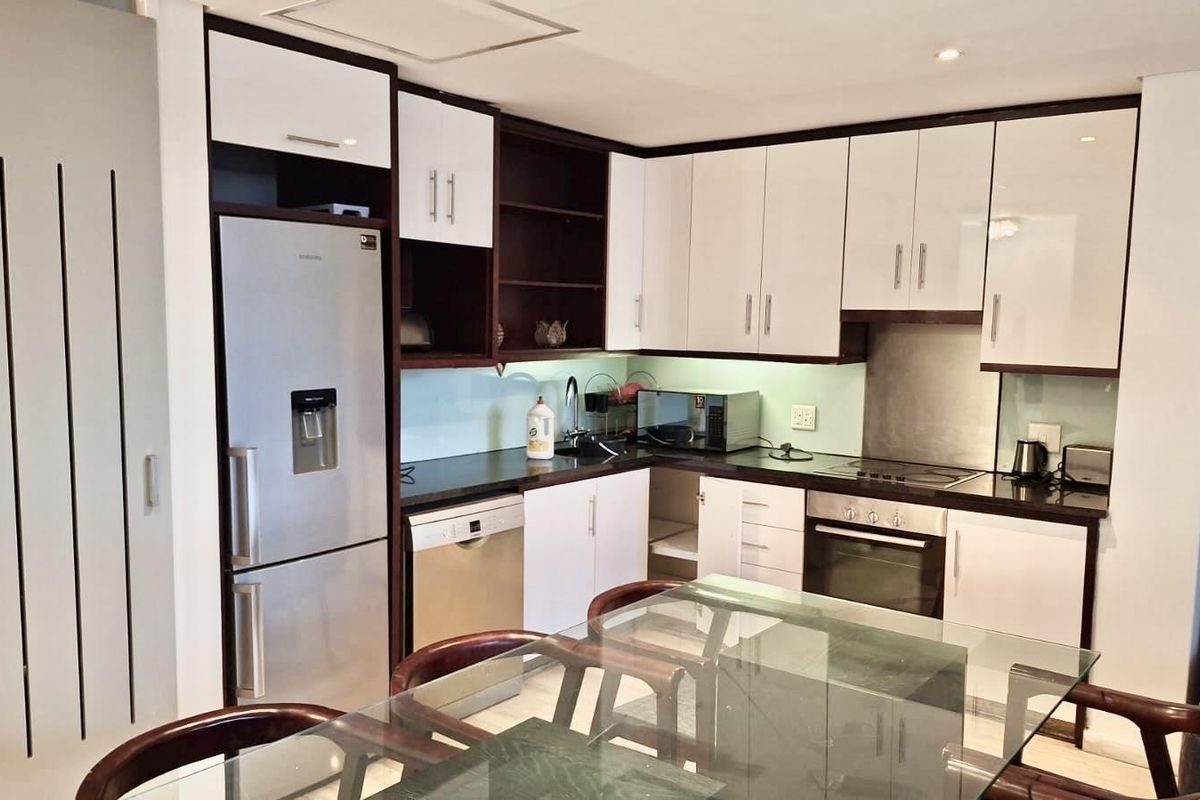 Modern kitchen featuring high-gloss white cabinetry, dark countertops, integrated appliances, and a sleek glass splashback, offering a clean and functional cooking space.