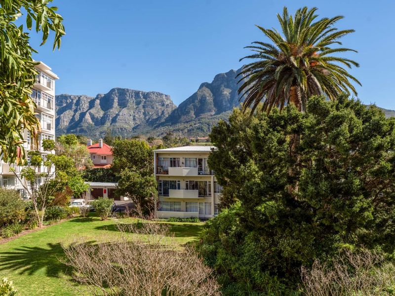 Scenic view of a well-maintained apartment complex surrounded by lush greenery and mature trees, set against a dramatic mountain backdrop.
