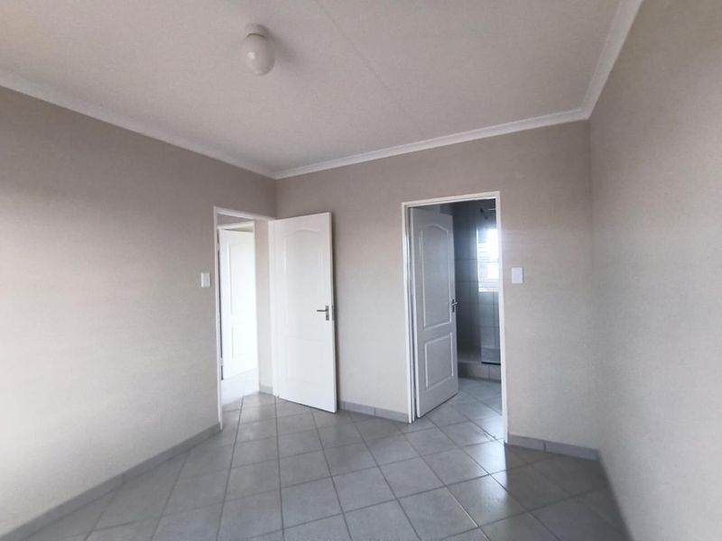 A clean, empty bedroom featuring neutral wall paint, tiled flooring, and coved ceilings, with direct access to an adjoining bathroom.