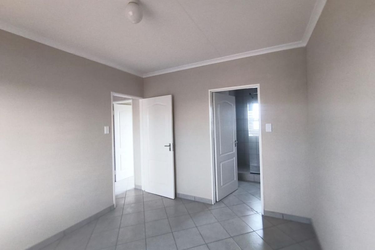A clean, empty bedroom featuring neutral wall paint, tiled flooring, and coved ceilings, with direct access to an adjoining bathroom.