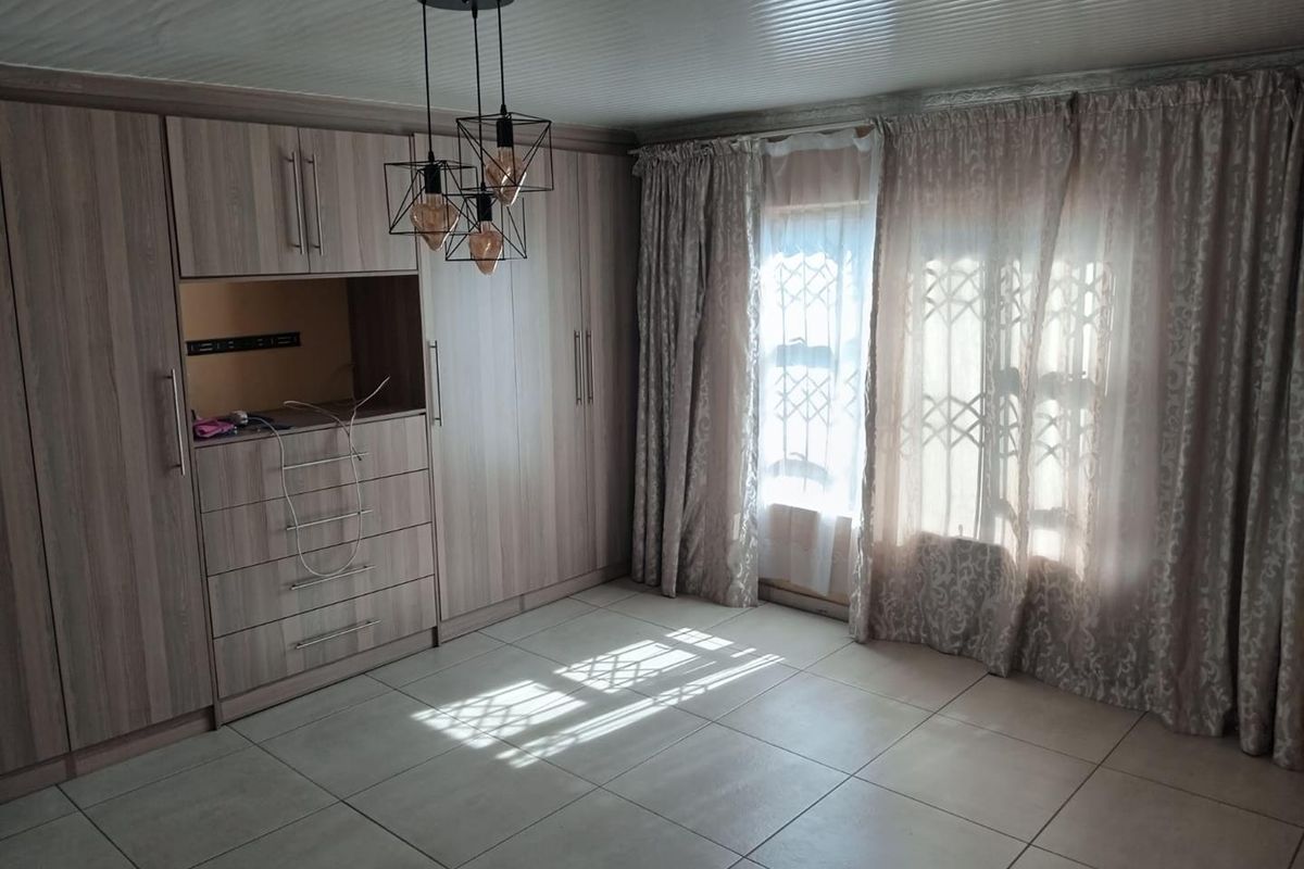 A spacious bedroom featuring extensive built-in cupboards, tiled flooring, and modern pendant lighting, offering a clean and functional living space.