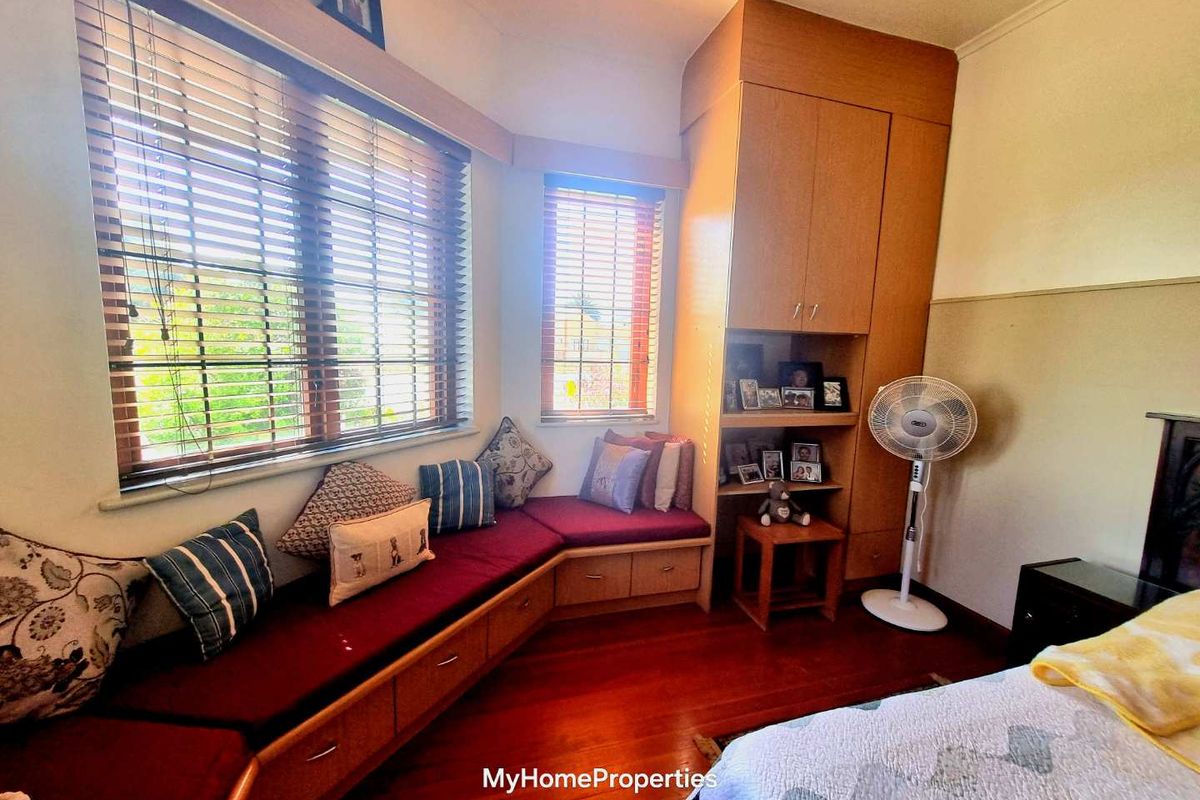 A bedroom featuring built-in wooden cabinetry, a corner window seat with storage, and polished timber flooring.