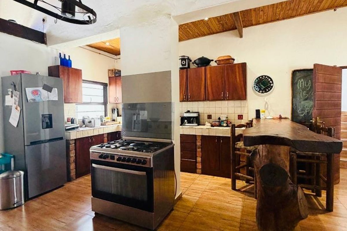 Spacious kitchen featuring wooden cabinetry, tiled flooring, and a freestanding gas stove under an exposed beam and thatch ceiling.