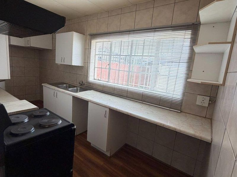 A functional kitchen featuring laminate countertops, a stainless steel double sink, built-in cabinetry, and a tiled splashback, offering a blank canvas for renovation.