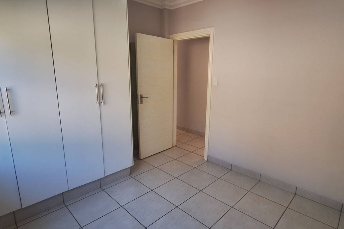 A clean, empty bedroom featuring neutral tiled flooring and ample built-in cupboard storage, ready for personalization.