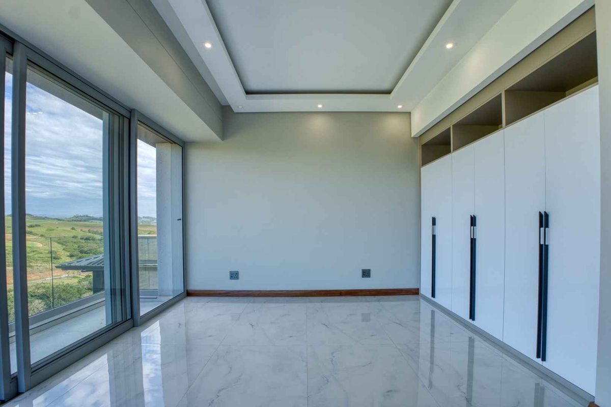Spacious bedroom featuring modern floor-to-ceiling glass sliding doors, built-in cabinetry with overhead storage, recessed ceiling lighting, and polished marble-look floor tiles.