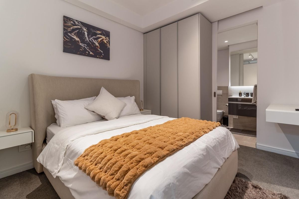 Modern bedroom featuring built-in floor-to-ceiling wardrobes and an en-suite bathroom with a vanity and mirror.