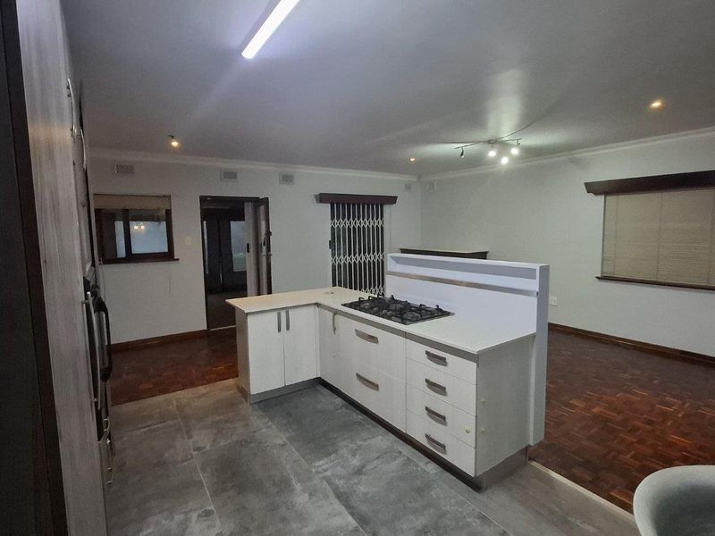 Open plan kitchen and living area featuring a central island with gas hob, parquet flooring, and neutral wall finishes.