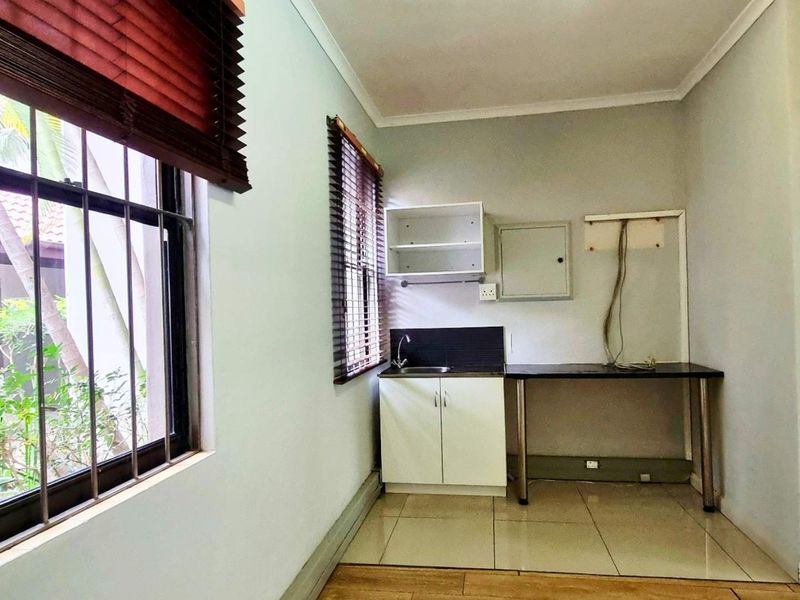 A functional scullery or kitchenette area featuring built-in cabinetry, a sink, tiled flooring, and natural light from windows with fitted blinds.