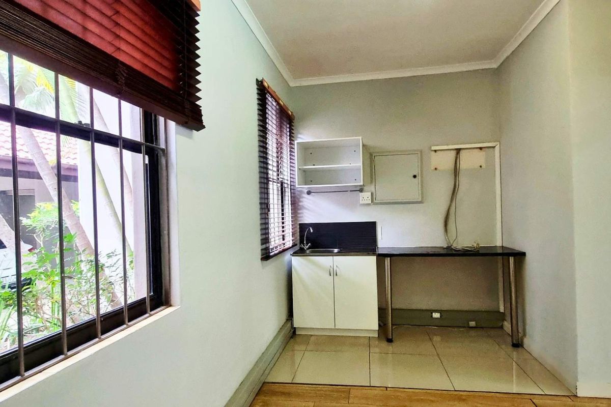 A functional scullery or kitchenette area featuring built-in cabinetry, a sink, tiled flooring, and natural light from windows with fitted blinds.
