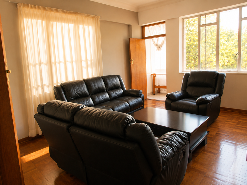 A bright living room featuring classic parquet flooring, large windows allowing ample natural light, and direct access to an adjoining balcony area.