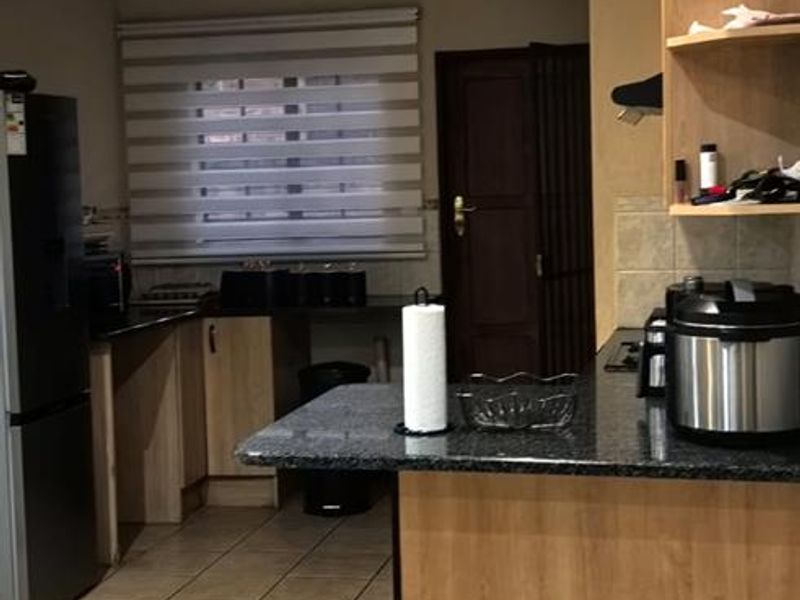 A functional kitchen featuring granite countertops, light wood-finish cabinetry, and tiled flooring with open shelving for storage.