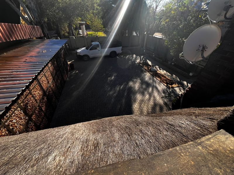 An elevated view of a paved rear courtyard area featuring a thatched roof section, boundary wall, and corrugated metal roofing structure.