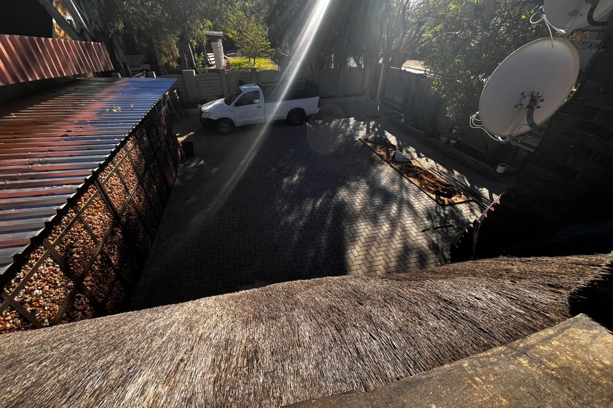 An elevated view of a paved rear courtyard area featuring a thatched roof section, boundary wall, and corrugated metal roofing structure.