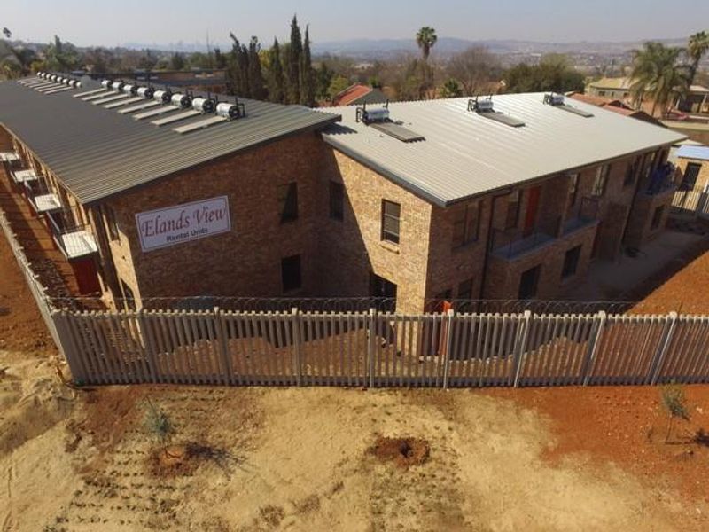 Aerial view of the Elands View apartment complex featuring facebrick construction, metal roofing with solar water heaters, and perimeter security fencing.