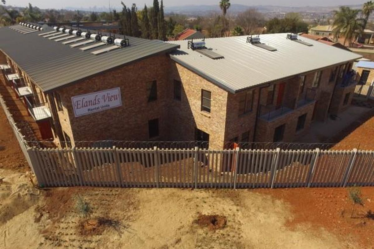 Aerial view of the Elands View apartment complex featuring facebrick construction, metal roofing with solar water heaters, and perimeter security fencing.