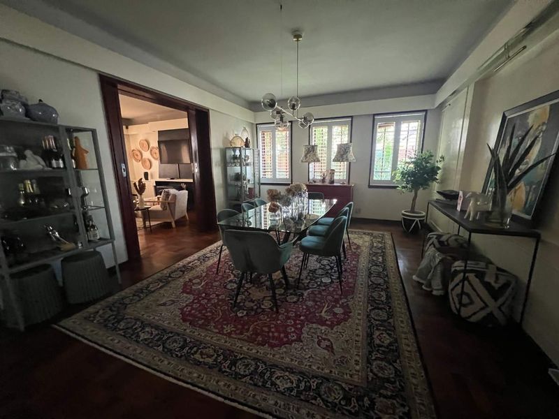 Spacious dining room featuring polished hardwood flooring, classic timber window shutters, and a large opening leading to the adjacent living area.