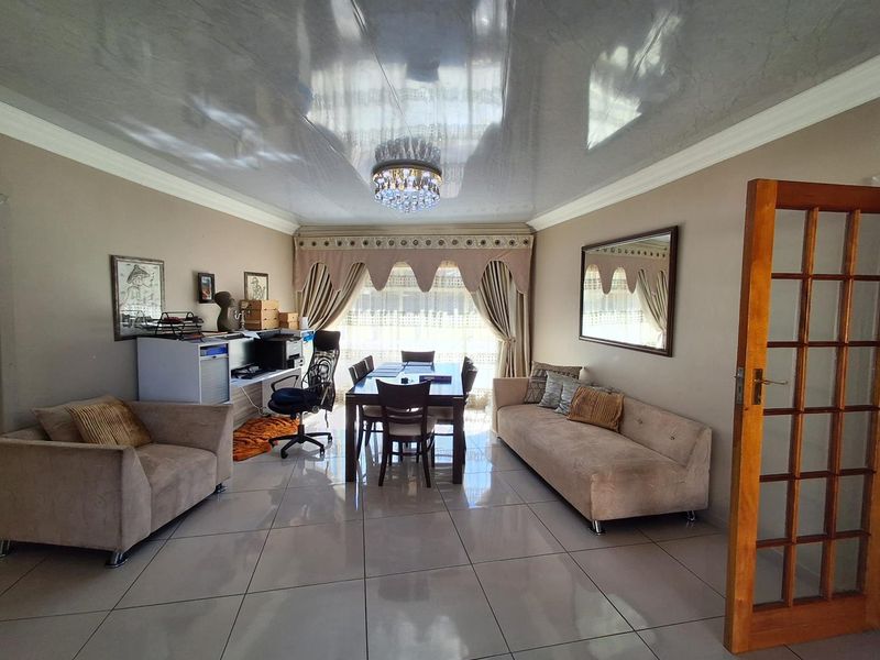 Spacious open-plan living and dining area featuring high-gloss ceiling finishes, polished porcelain floor tiles, and a decorative crystal chandelier.