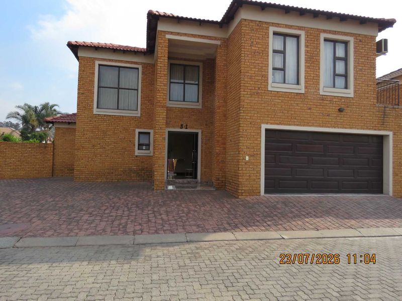 A double-storey face-brick cluster home featuring a paved driveway, double garage, and a tiled roof.
