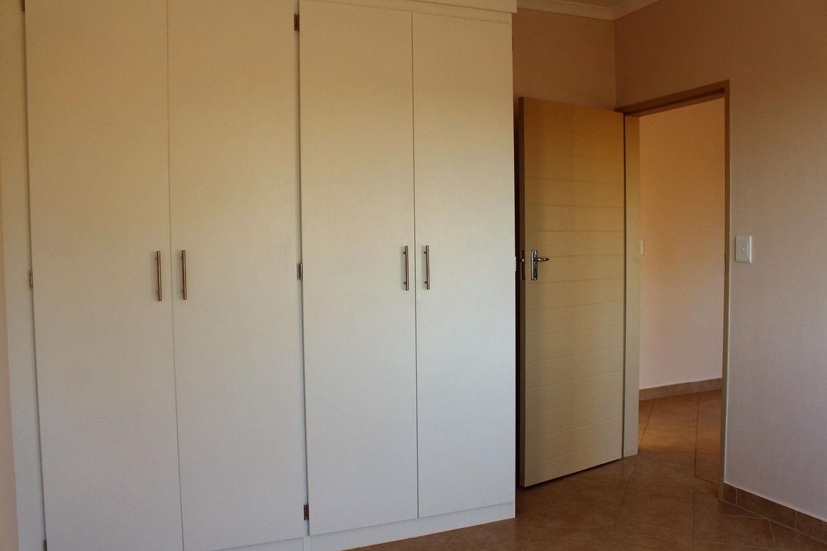 A clean bedroom interior featuring white built-in cupboards, tiled flooring, and a neutral color palette, offering a functional and well-maintained space.