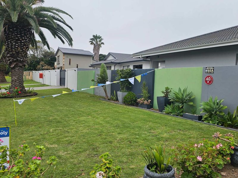 A well-maintained front exterior view featuring a landscaped lawn, modern boundary wall, and paved driveway access.