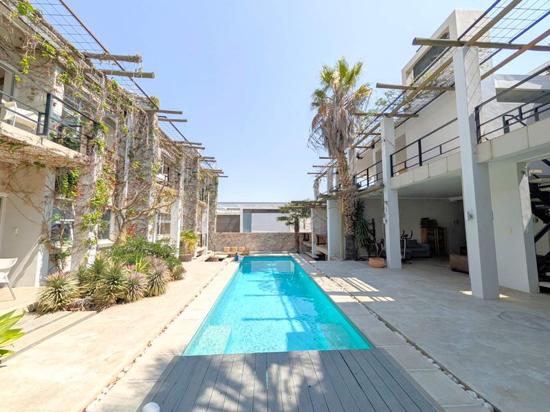 A central swimming pool area flanked by multi-story guest house wings featuring stone-clad walls, timber pergolas, and covered patio spaces.