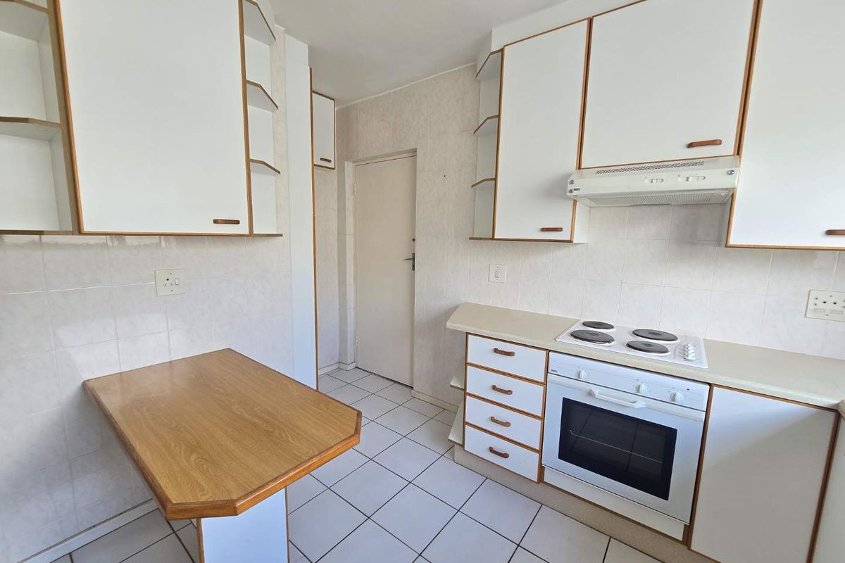 A functional kitchen featuring white cabinetry, a built-in oven and hob, tiled flooring, and a small integrated breakfast counter.