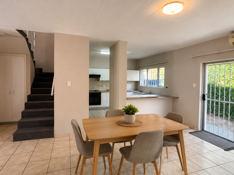 Open-plan living and dining area featuring tiled floors, a staircase, and a functional kitchen with built-in cabinetry, leading to an outdoor patio area.