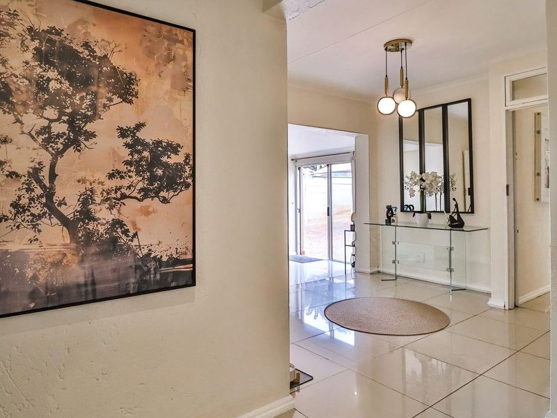 A bright and welcoming entrance hall featuring polished tiled flooring, modern pendant lighting, and a clear view through to the rear outdoor area.