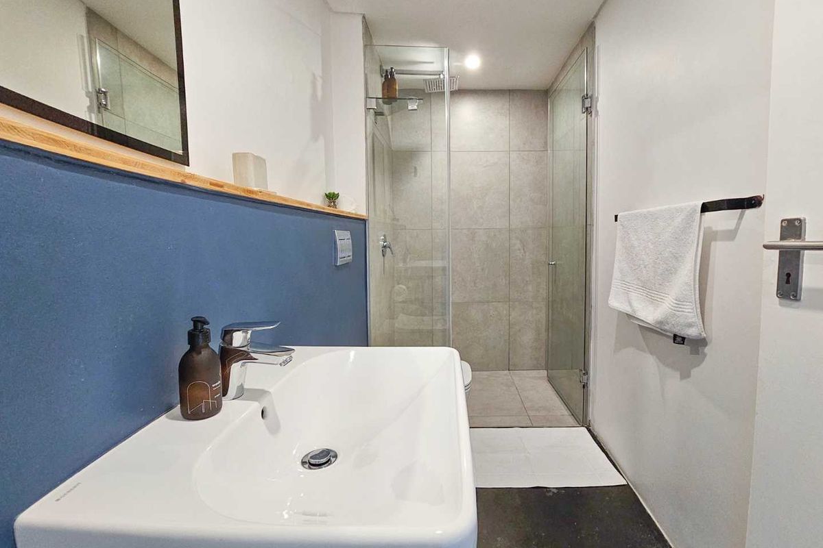 Modern bathroom featuring a wall-mounted basin, glass-enclosed walk-in shower with large format tiling, and contemporary blue accent wall.
