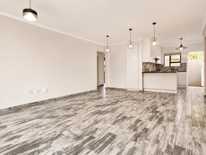 Spacious open-plan living area featuring modern tiled flooring, contemporary pendant lighting, and a sleek, well-appointed kitchen with built-in appliances.
