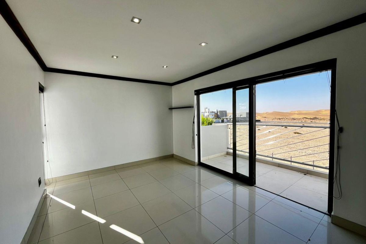 Bright, empty living area featuring large sliding glass doors that open onto a balcony with scenic desert views and tiled flooring throughout.