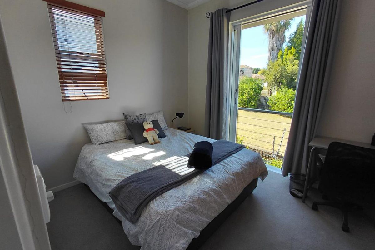 A well-lit bedroom featuring carpeted flooring, a sliding glass door leading to an outdoor area, and fitted window treatments.