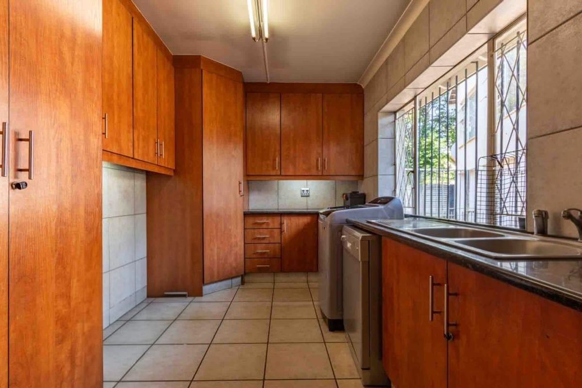 A functional kitchen featuring wood-finish cabinetry, tiled flooring, double stainless steel sink, and integrated space for laundry appliances.