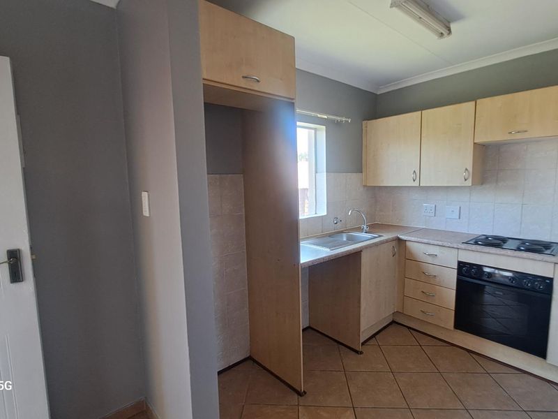 A functional kitchen featuring light wood-finish cabinetry, laminate countertops, a built-in oven with hob, and tiled flooring.